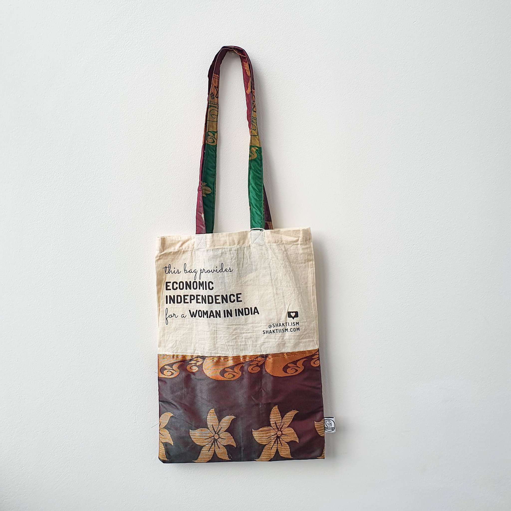 A vibrant Independence sari tote bag handcrafted from repurposed sari fabric, showcasing unique patterns and colors, with a message promoting women's economic independence.