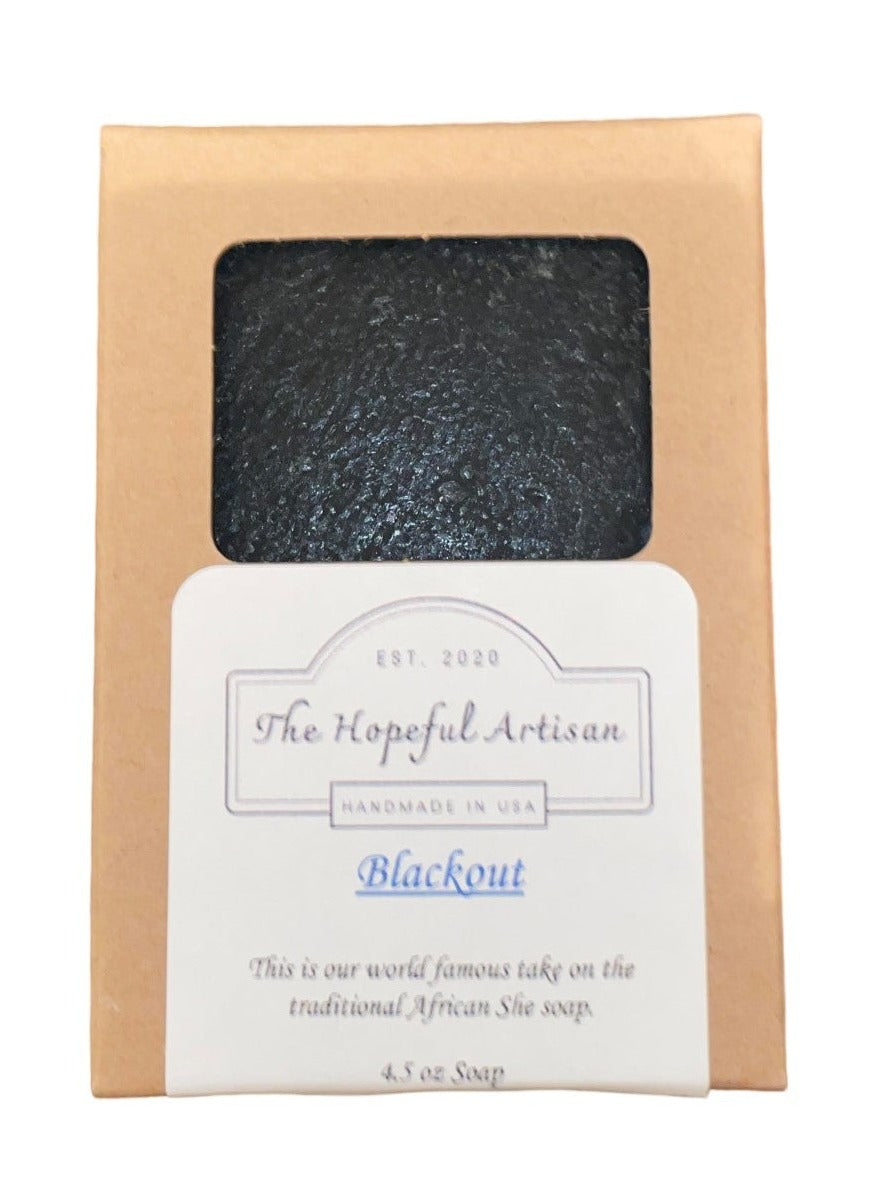 Blackout Shea soap bar with activated charcoal, featuring oakmoss and aloe fragrance, displayed on a natural wooden surface.