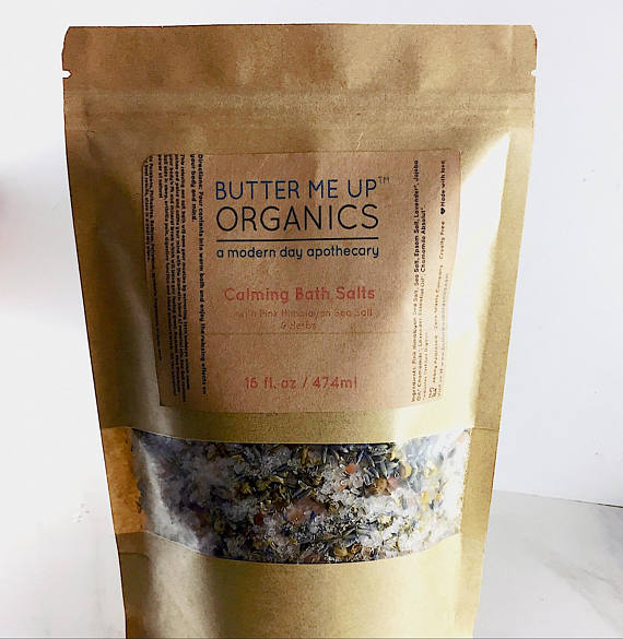 A resealable kraft glassine bag filled with Calming Bath Salts, featuring a blend of Epsom, Pink Himalayan, and Sea Salts, infused with lavender and chamomile.