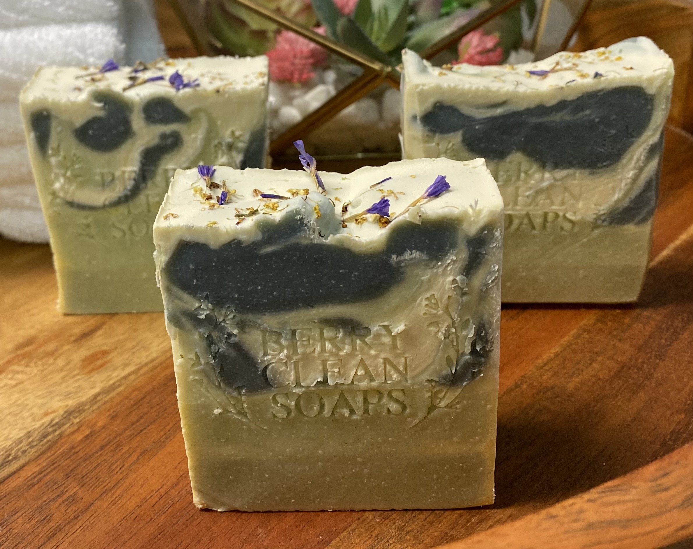 A beautifully crafted indigo soap bar showcasing a blend of blue and green hues, with visible spices and fruit elements, resting on a wooden surface.