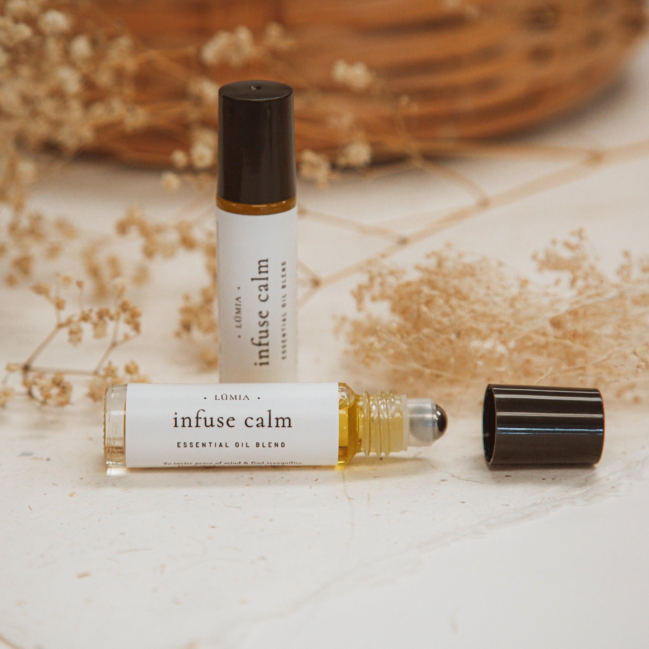 Infuse Calm essential oil blend in a small glass bottle with a dropper, surrounded by calming herbs and flowers.