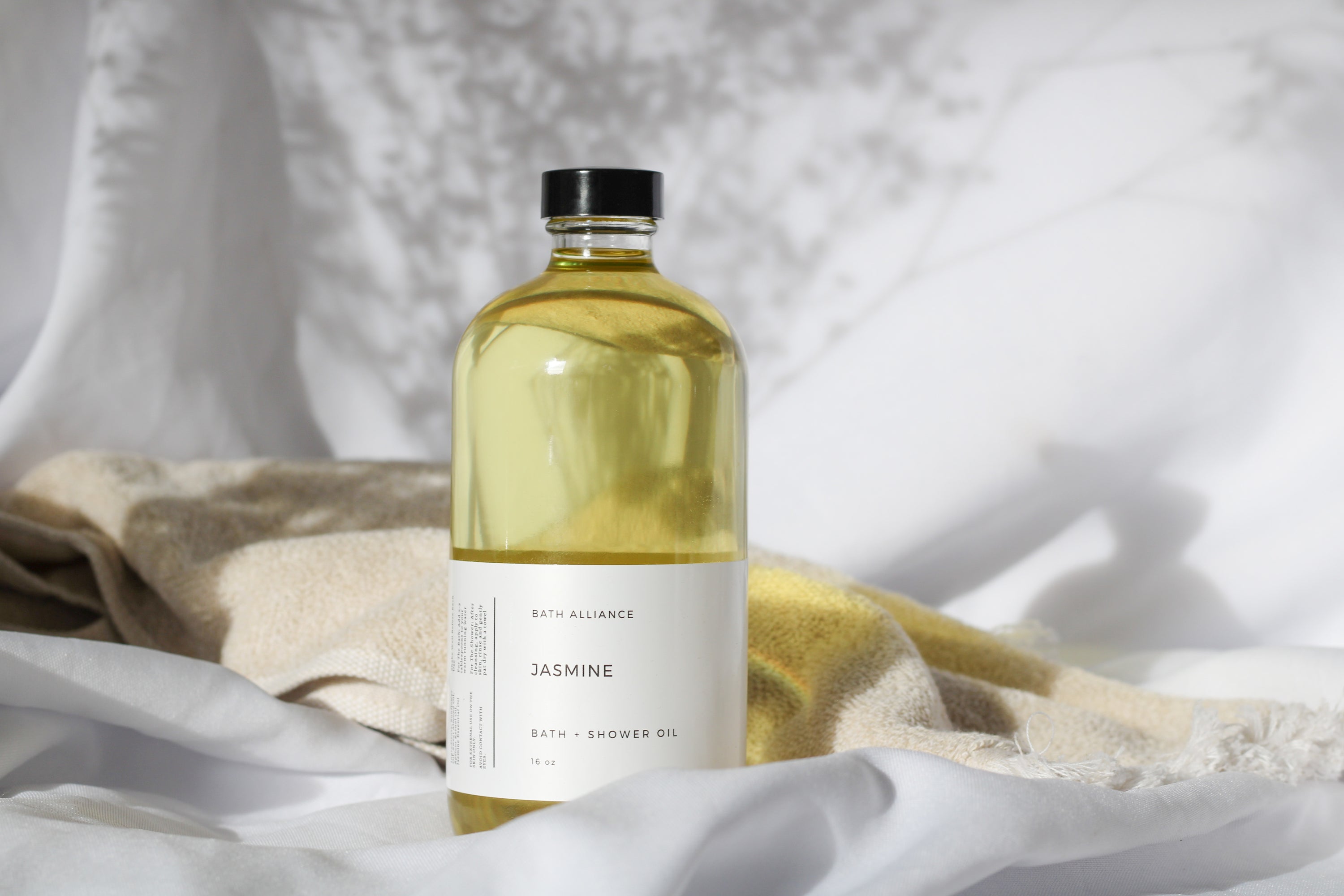 A luxurious bottle of Jasmine Bath + Shower Oil surrounded by jasmine flowers, showcasing its elegant design and natural ingredients.