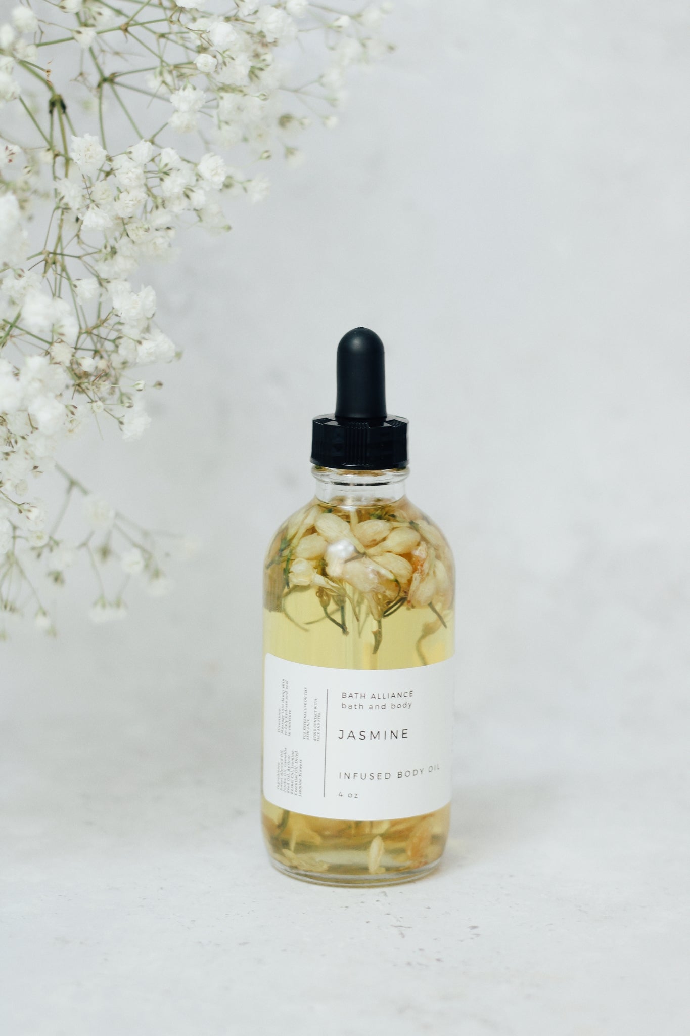 A luxurious jar of Jasmine Body Oil featuring a blend of natural oils, surrounded by dried jasmine flowers.