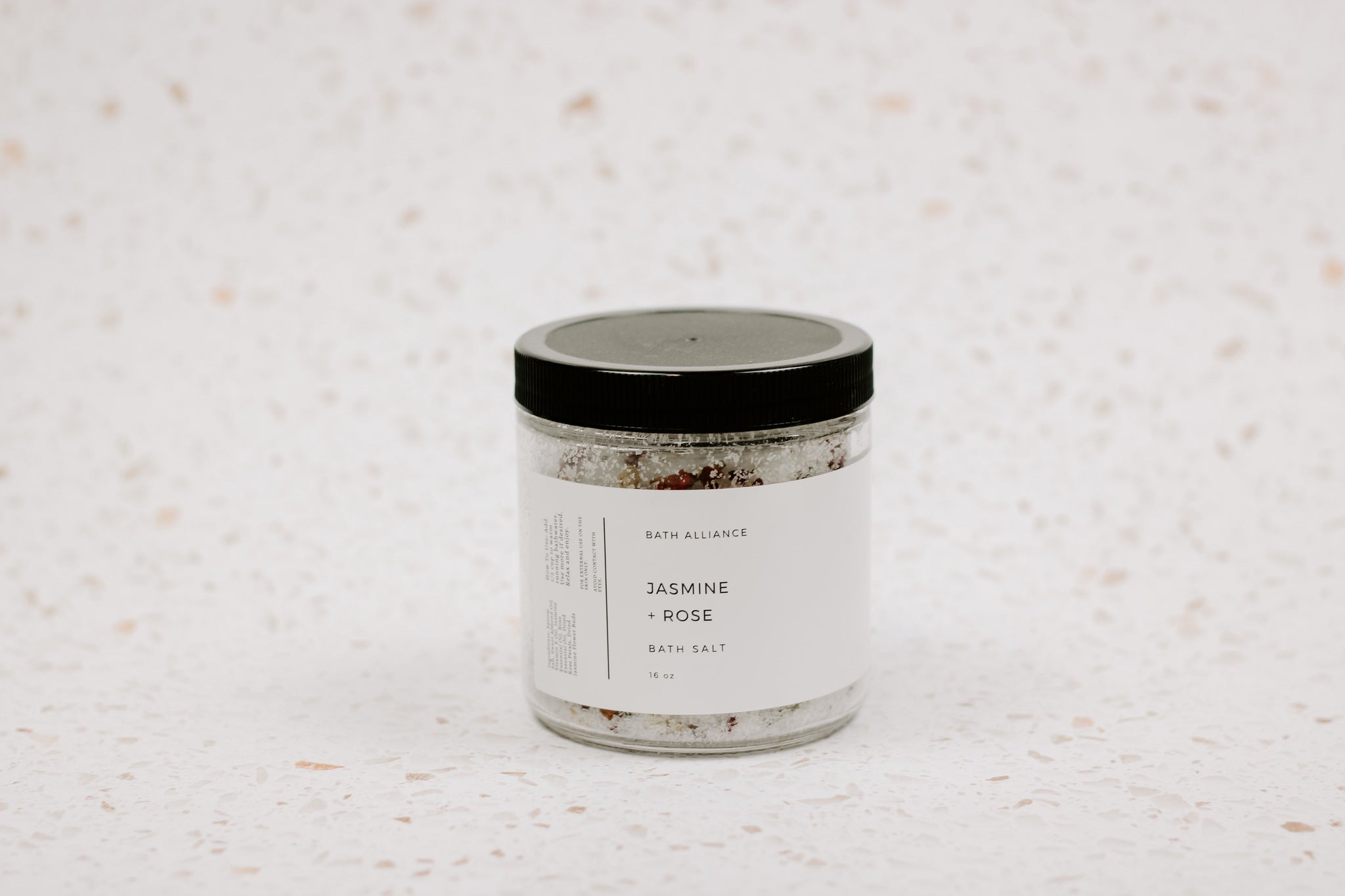 A beautifully arranged jar of Jasmine + Rose Bath Salt with dried rose petals and jasmine flower buds, showcasing its natural ingredients.