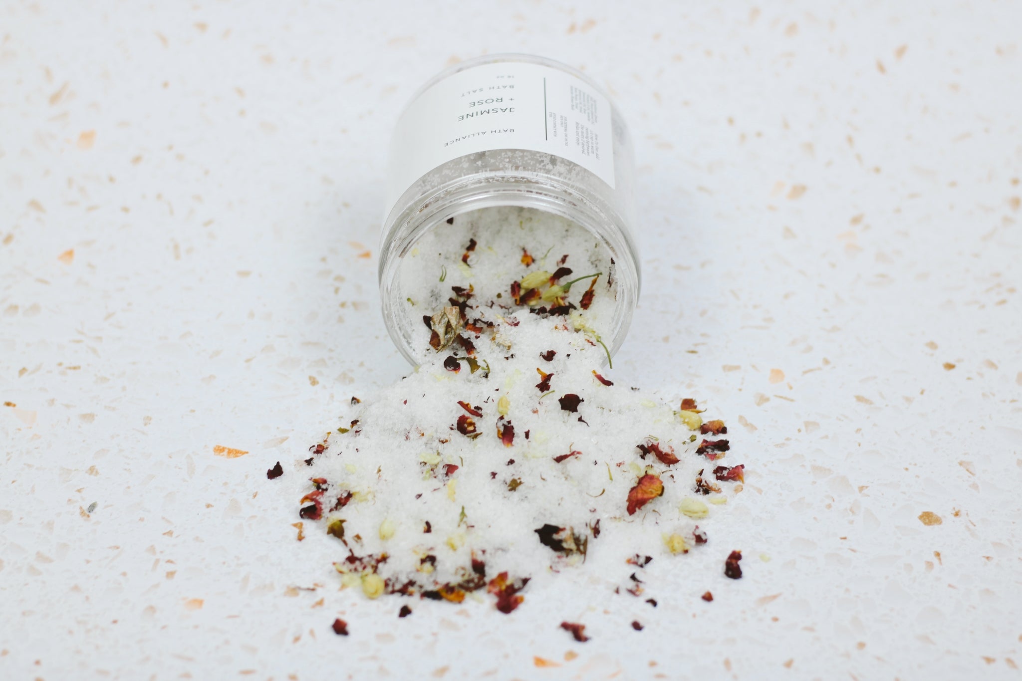 A beautifully arranged jar of Jasmine + Rose Bath Salt with dried rose petals and jasmine flower buds, showcasing its natural ingredients.