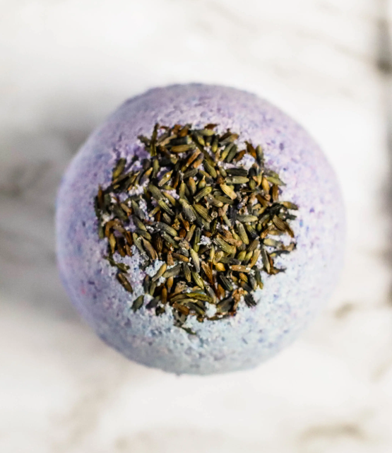 A large lavender bath bomb, 7oz, with a vibrant purple color, surrounded by dried lavender flowers, showcasing its natural ingredients.