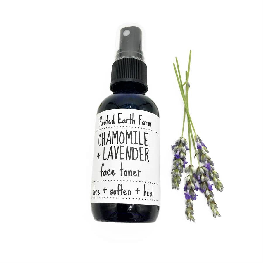 A cobalt blue glass spray bottle containing Lavender & Chamomile Face Toner, surrounded by lavender and chamomile flowers.