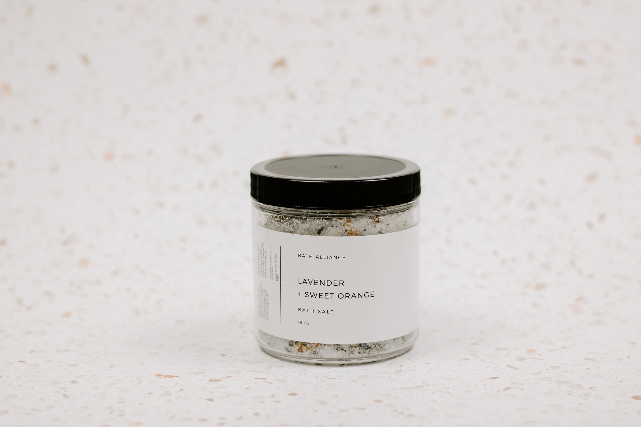 A jar of Lavender + Sweet Orange Bath Salt with dried lavender buds and orange peels, showcasing its natural ingredients.