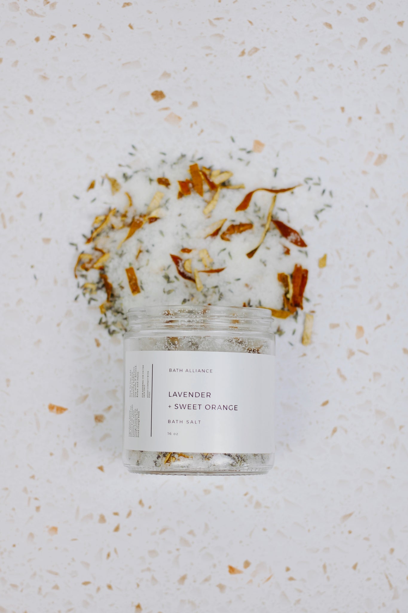 A jar of Lavender + Sweet Orange Bath Salt with dried lavender buds and orange peels, showcasing its natural ingredients.