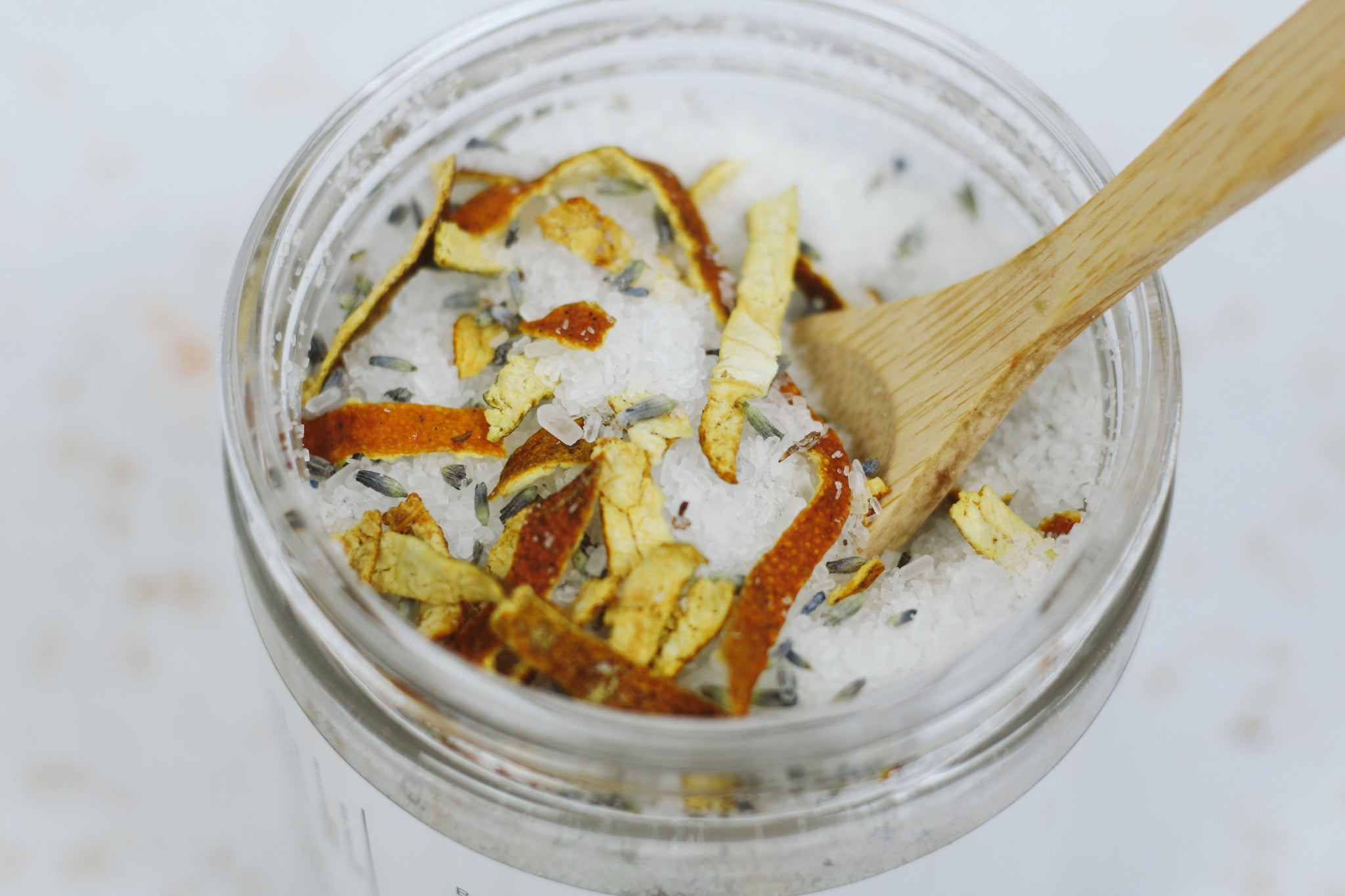 A jar of Lavender + Sweet Orange Bath Salt with dried lavender buds and orange peels, showcasing its natural ingredients.