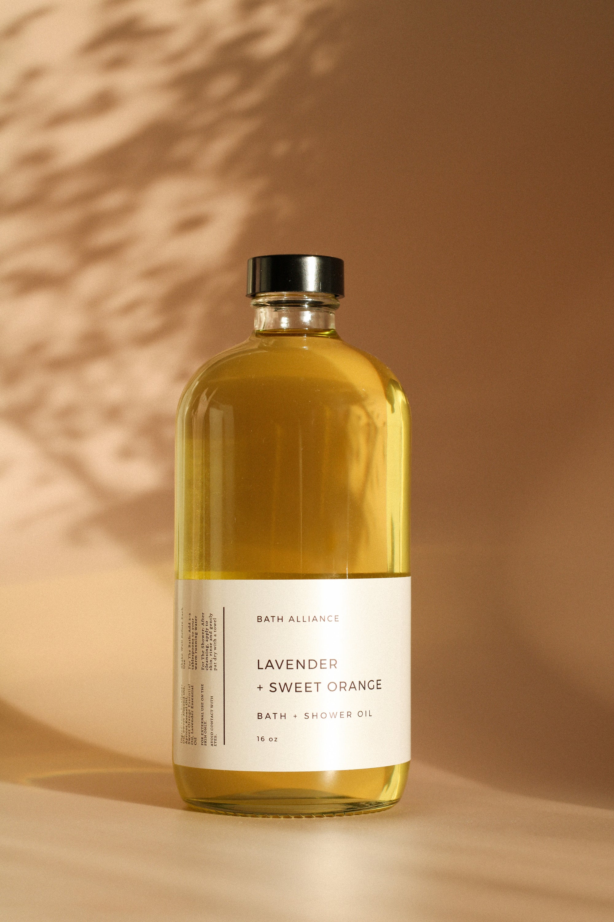 A 16 oz glass bottle of Lavender + Sweet Orange Bath + Shower Oil, showcasing its rich, golden color and elegant label design.