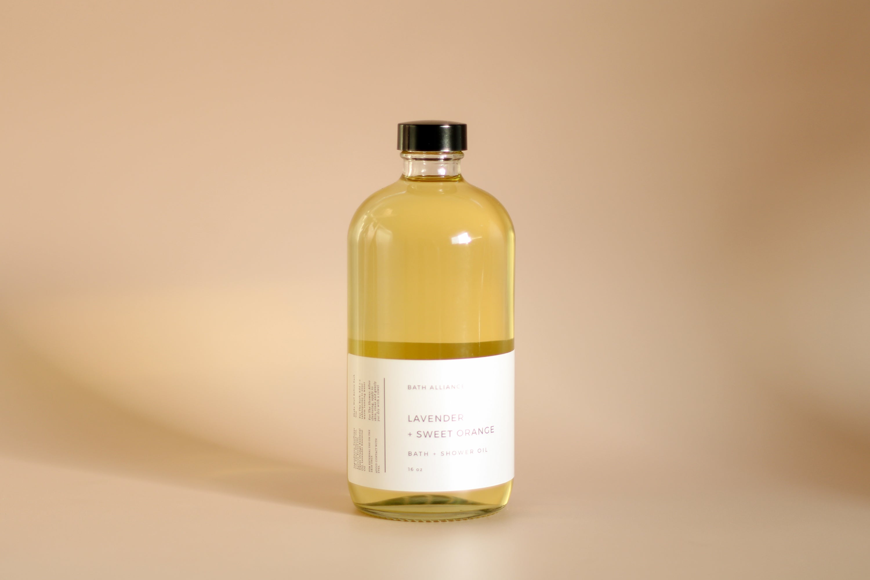 A 16 oz glass bottle of Lavender + Sweet Orange Bath + Shower Oil, showcasing its rich, golden color and elegant label design.