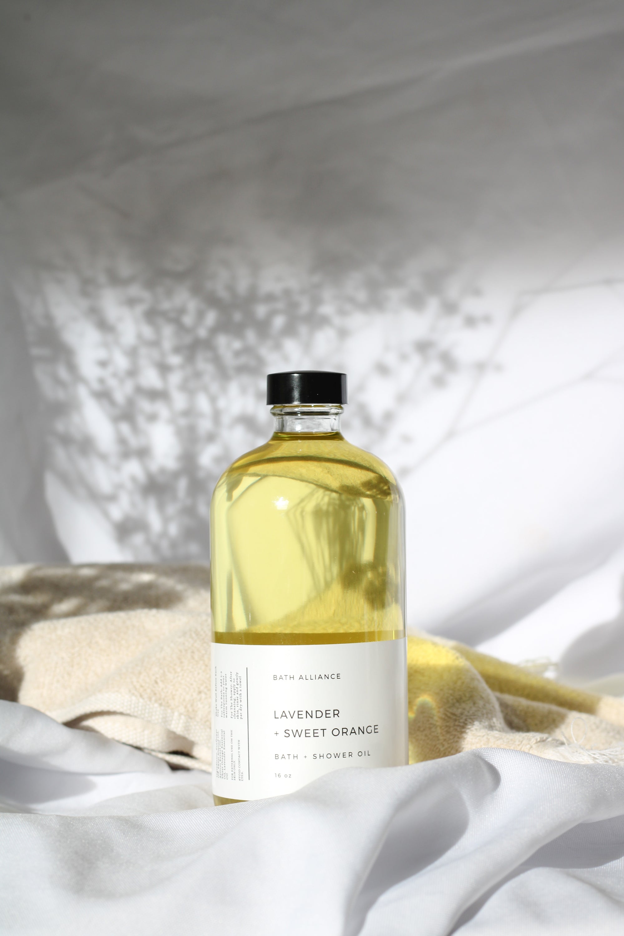 A 16 oz glass bottle of Lavender + Sweet Orange Bath + Shower Oil, showcasing its rich, golden color and elegant label design.