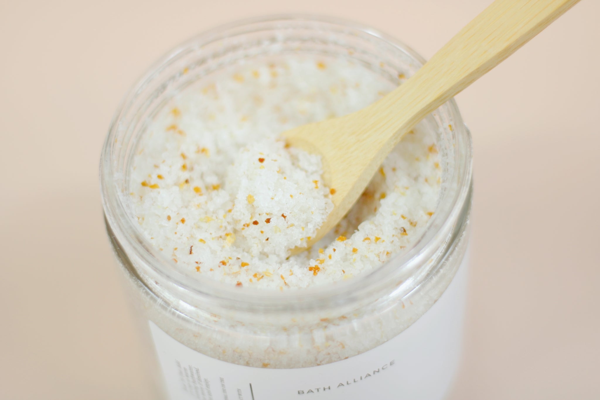 A jar of Lemon + Vanilla Bath Salt with a refreshing lemon and vanilla scent, surrounded by lemon slices and flowers.