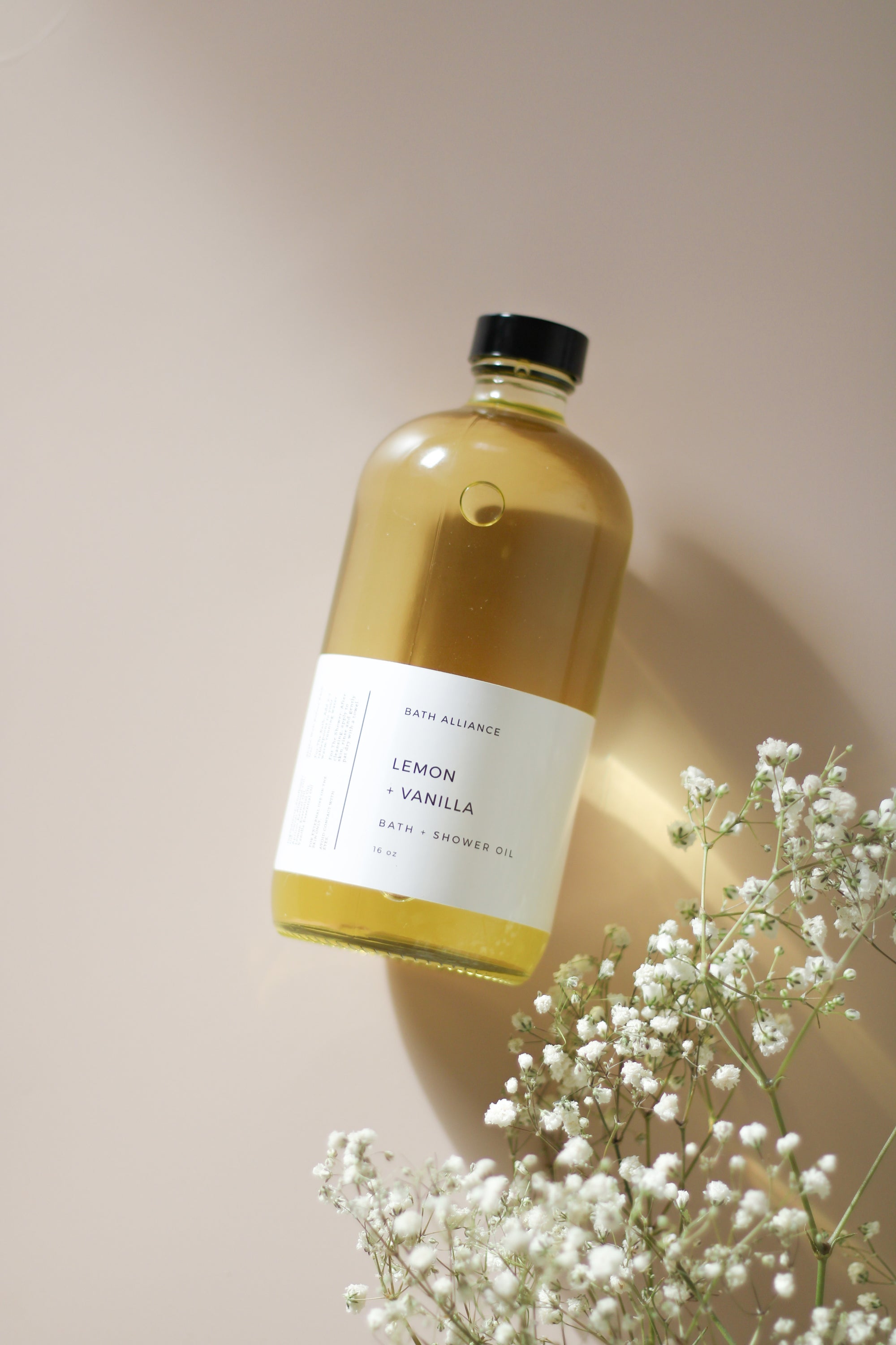 A 16 oz glass bottle of Lemon + Vanilla Bath + Shower Oil with a bright yellow label, showcasing its nourishing ingredients and refreshing aroma.