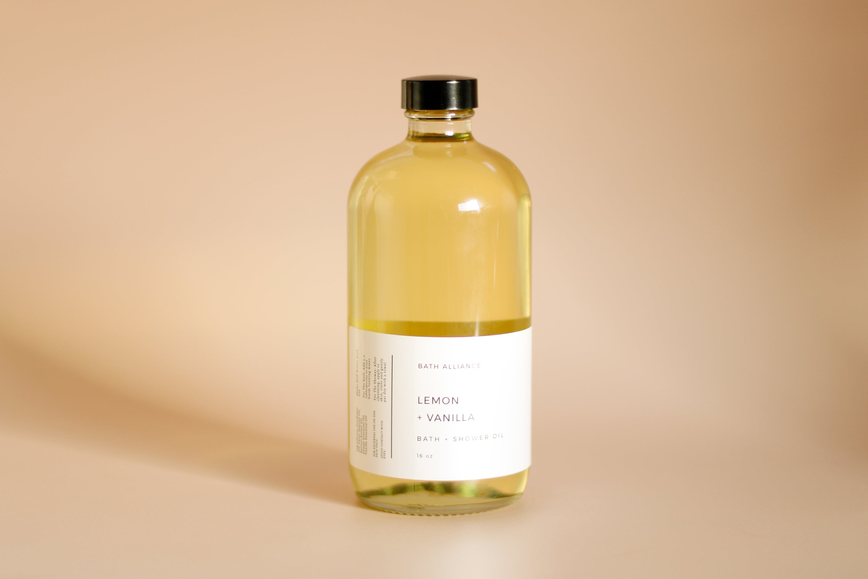 A 16 oz glass bottle of Lemon + Vanilla Bath + Shower Oil with a bright yellow label, showcasing its nourishing ingredients and refreshing aroma.