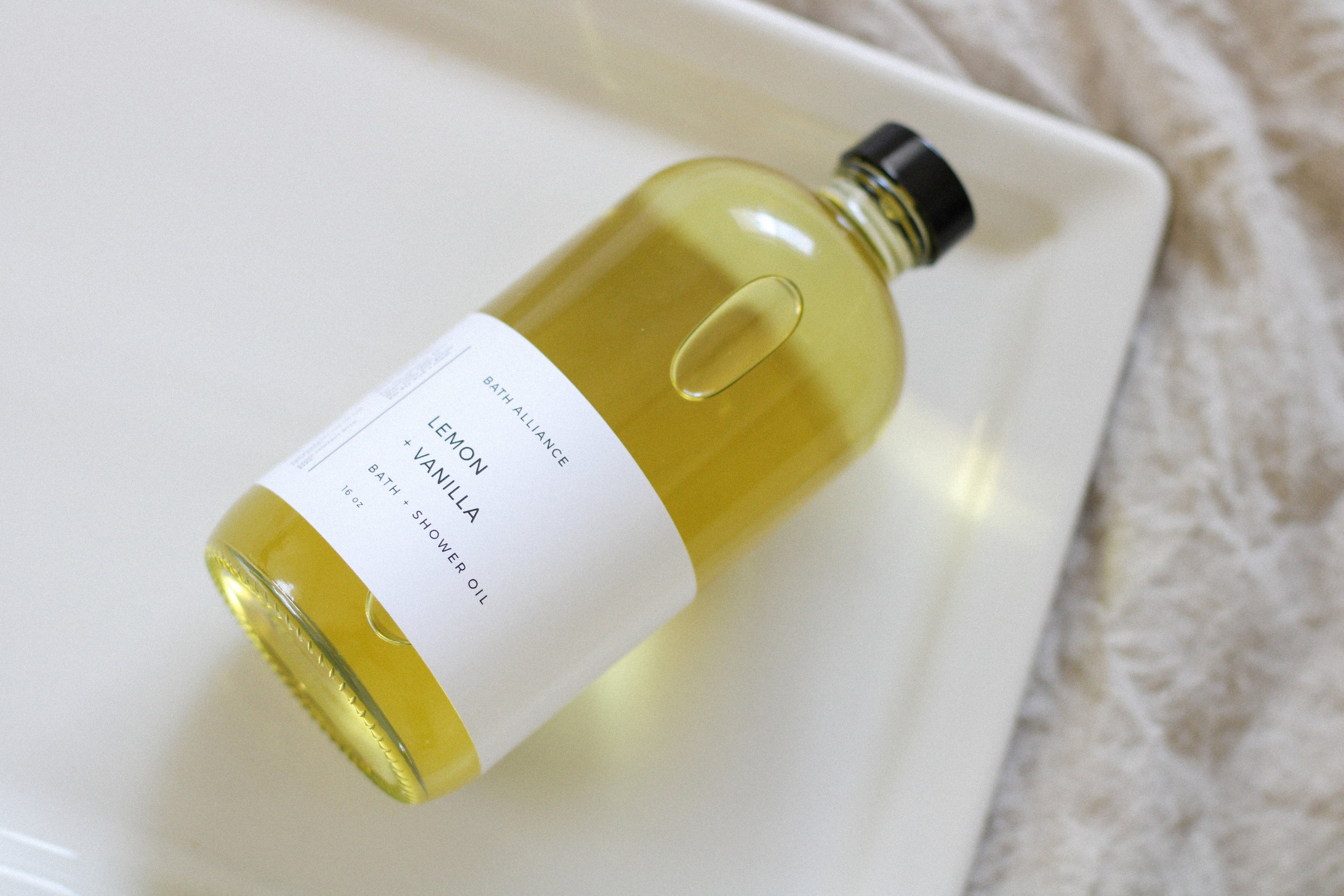 A 16 oz glass bottle of Lemon + Vanilla Bath + Shower Oil with a bright yellow label, showcasing its nourishing ingredients and refreshing aroma.