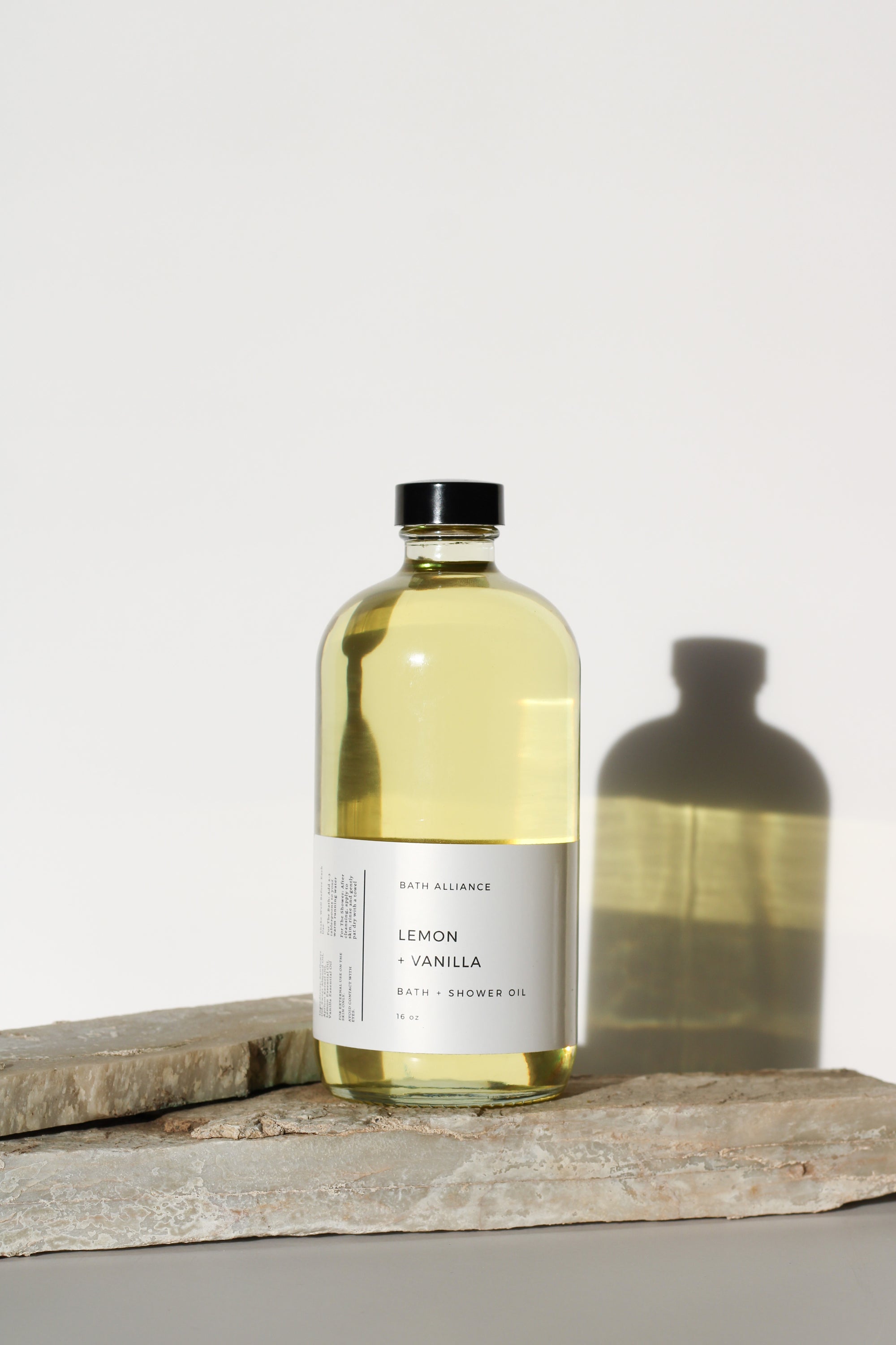 A 16 oz glass bottle of Lemon + Vanilla Bath + Shower Oil with a bright yellow label, showcasing its nourishing ingredients and refreshing aroma.