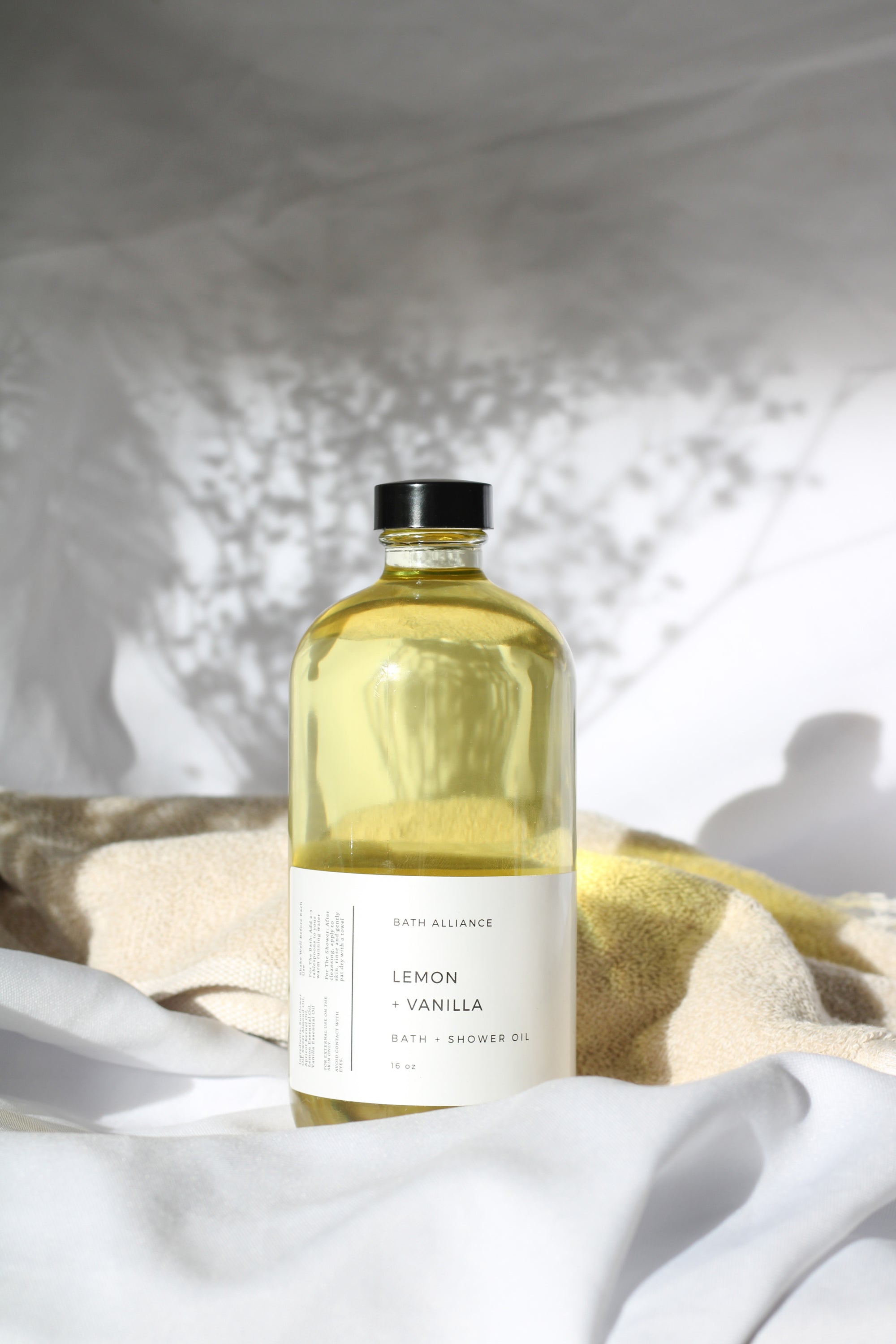 A 16 oz glass bottle of Lemon + Vanilla Bath + Shower Oil with a bright yellow label, showcasing its nourishing ingredients and refreshing aroma.