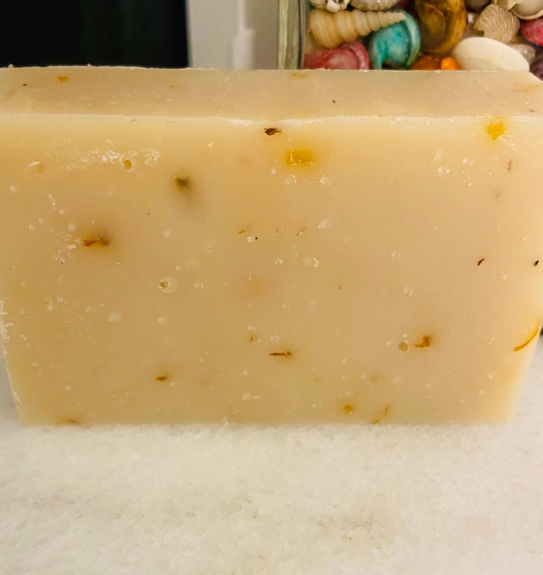 A bar of Pink Grapefruit Soap with a vibrant pink color, featuring calendula petals on top, resting on a wooden surface.