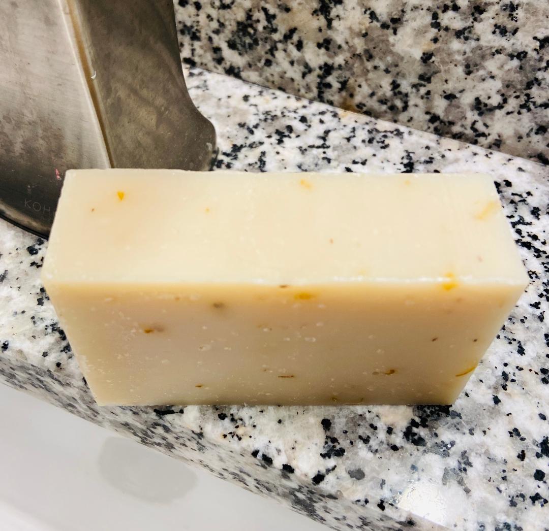 A bar of Pink Grapefruit Soap with a vibrant pink color, featuring calendula petals on top, resting on a wooden surface.