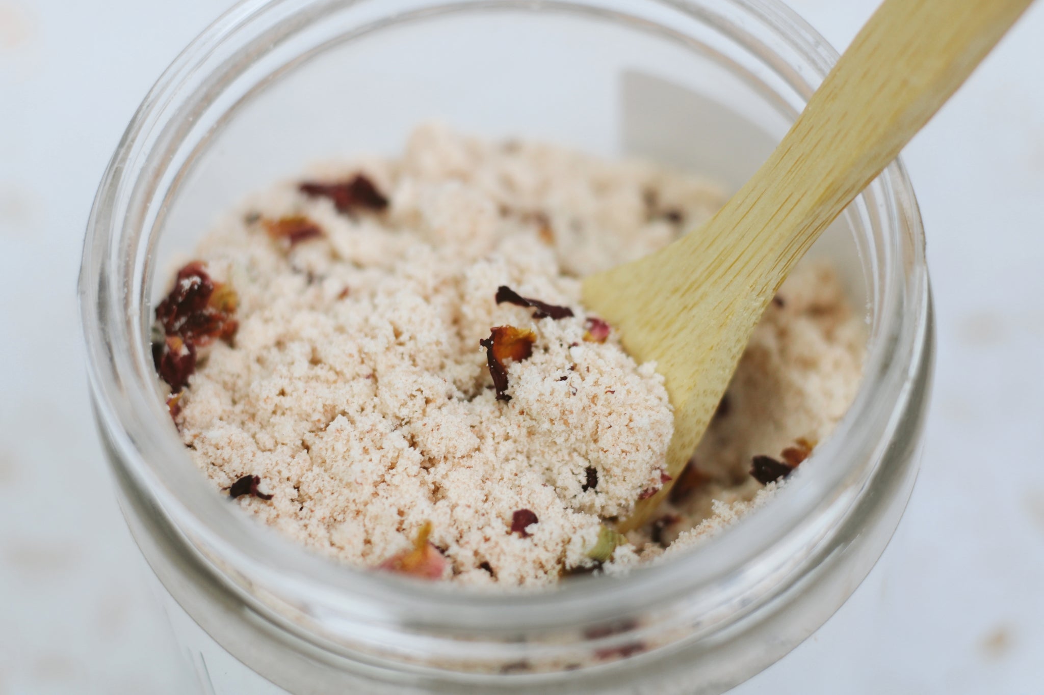 A jar of Rose + Coconut Milk Bath Soak featuring dried rose petals and powdered coconut milk, perfect for a relaxing bath experience.