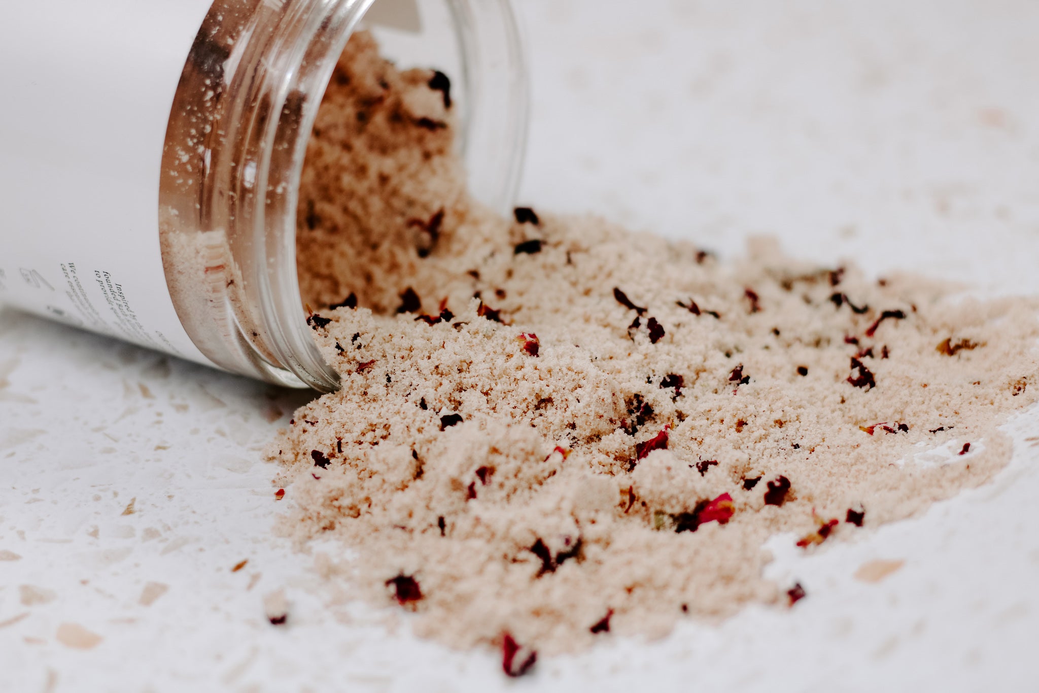 A jar of Rose + Coconut Milk Bath Soak featuring dried rose petals and powdered coconut milk, perfect for a relaxing bath experience.