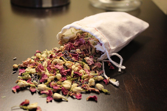 A muslin bag filled with organic bath tea, featuring pink rose petals, jasmine flowers, lavender, oatstraw, and burdock root powder, displayed elegantly.