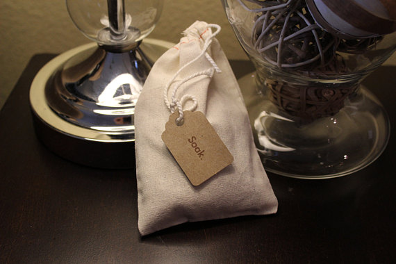 A muslin bag filled with organic bath tea, featuring pink rose petals, jasmine flowers, lavender, oatstraw, and burdock root powder, displayed elegantly.