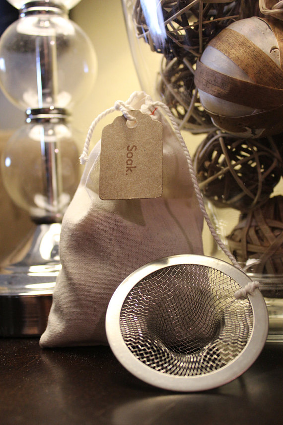 A muslin bag filled with organic bath tea, featuring pink rose petals, jasmine flowers, lavender, oatstraw, and burdock root powder, displayed elegantly.