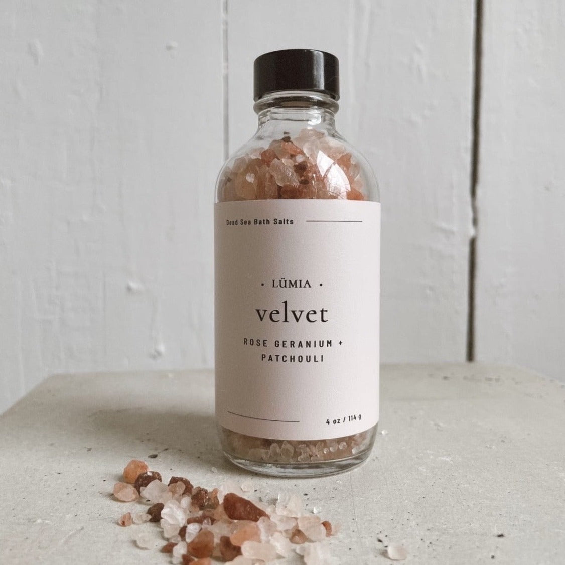 A jar of Velvet Bath Salts featuring pink Himalayan salt and essential oils, surrounded by rose petals and a calming ambiance.