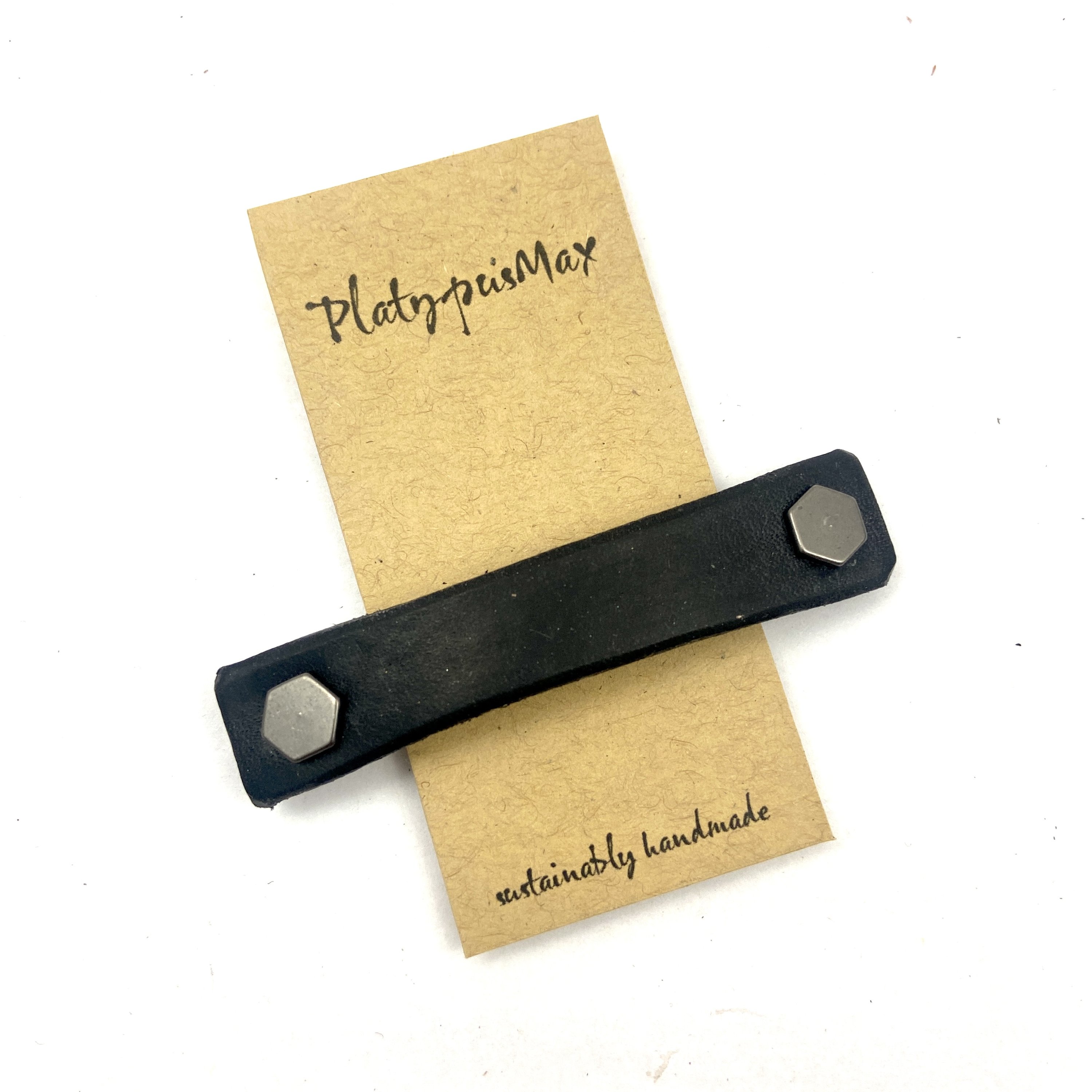 Black leather barrette with industrial hex hardware, showcasing eco-friendly design and sturdy metal clip.