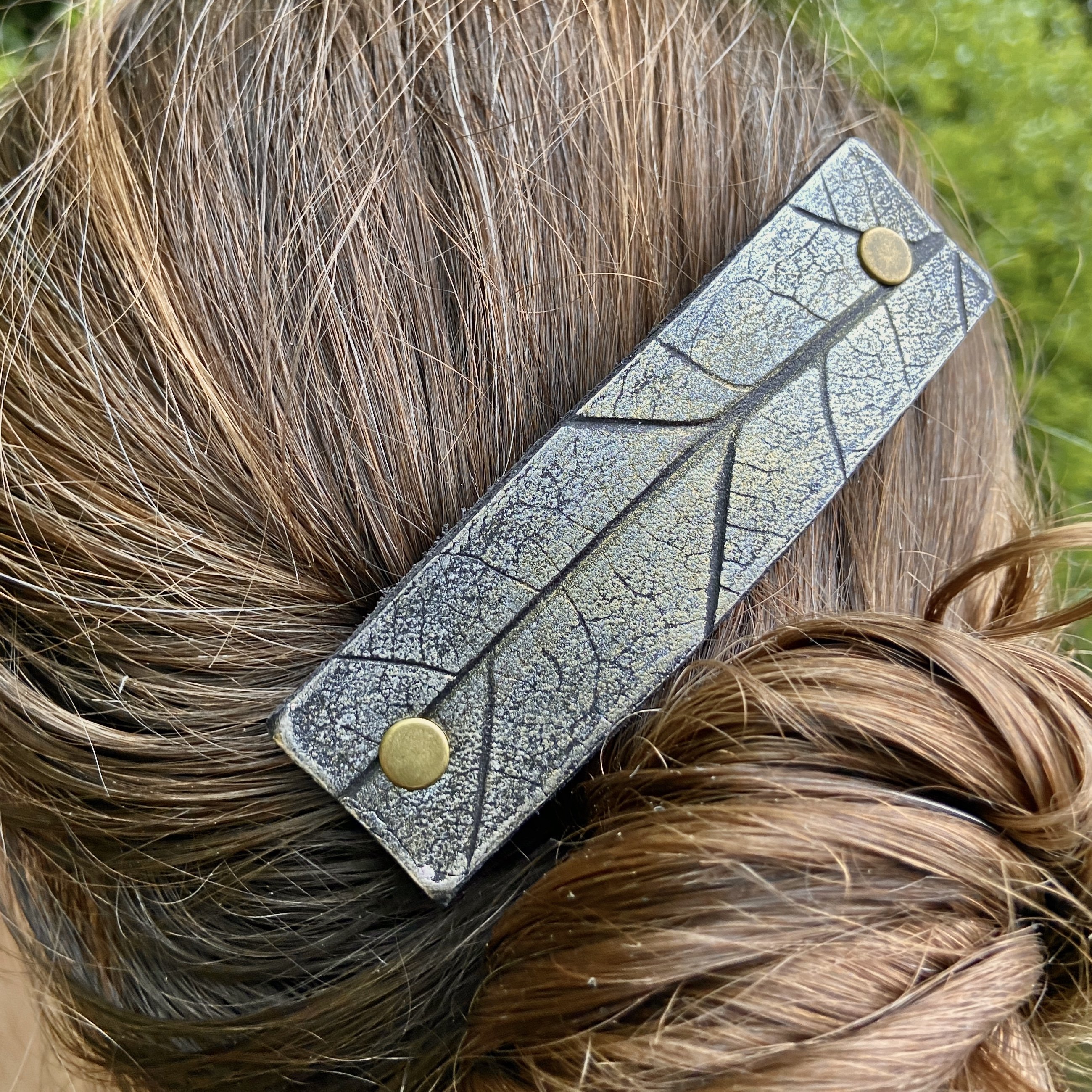 A handcrafted platinum oak leaf pressed leather hair barrette featuring an embossed leaf design on black-dyed leather.