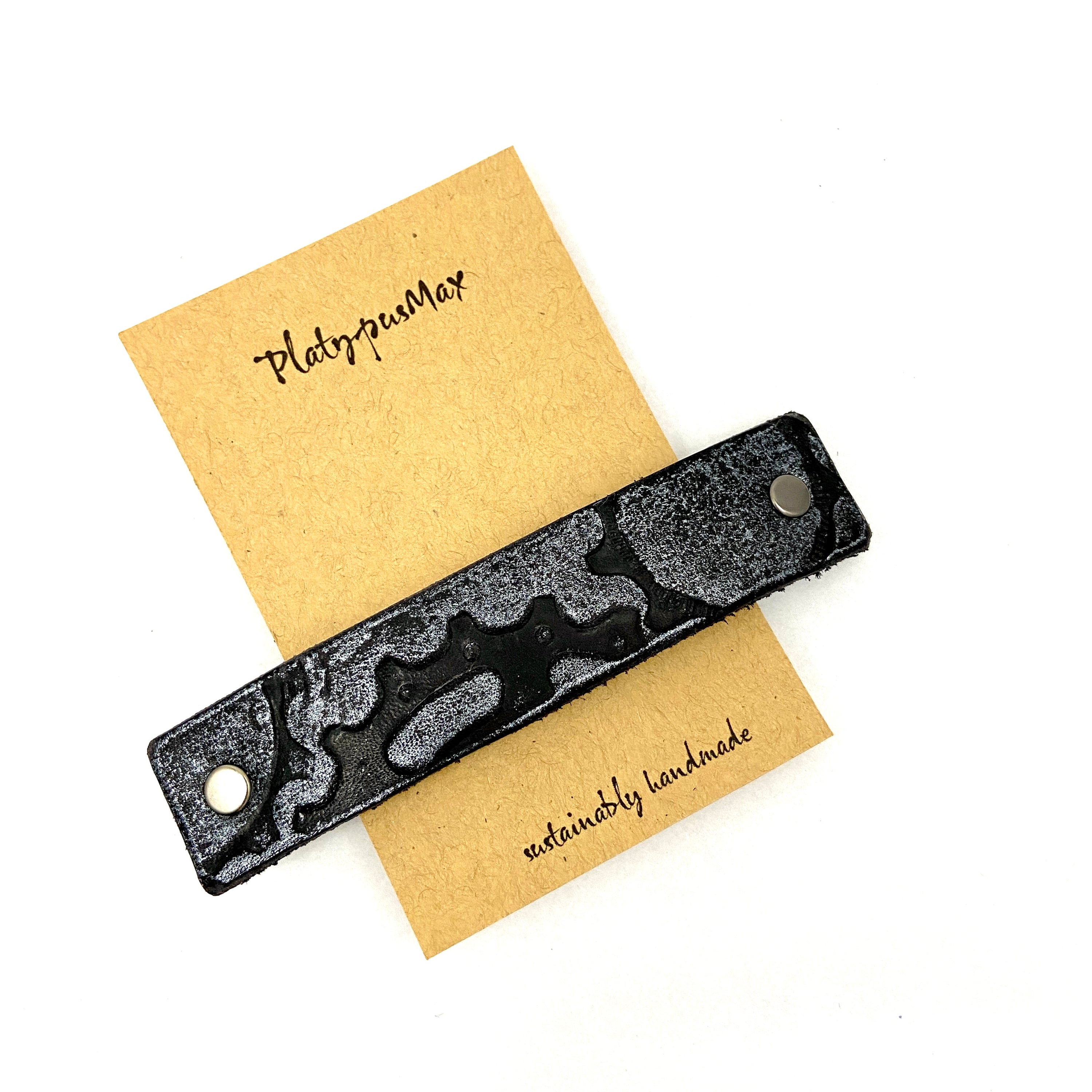 A stylish silver leather barrette featuring embossed bicycle gears, showcasing a unique steampunk design.