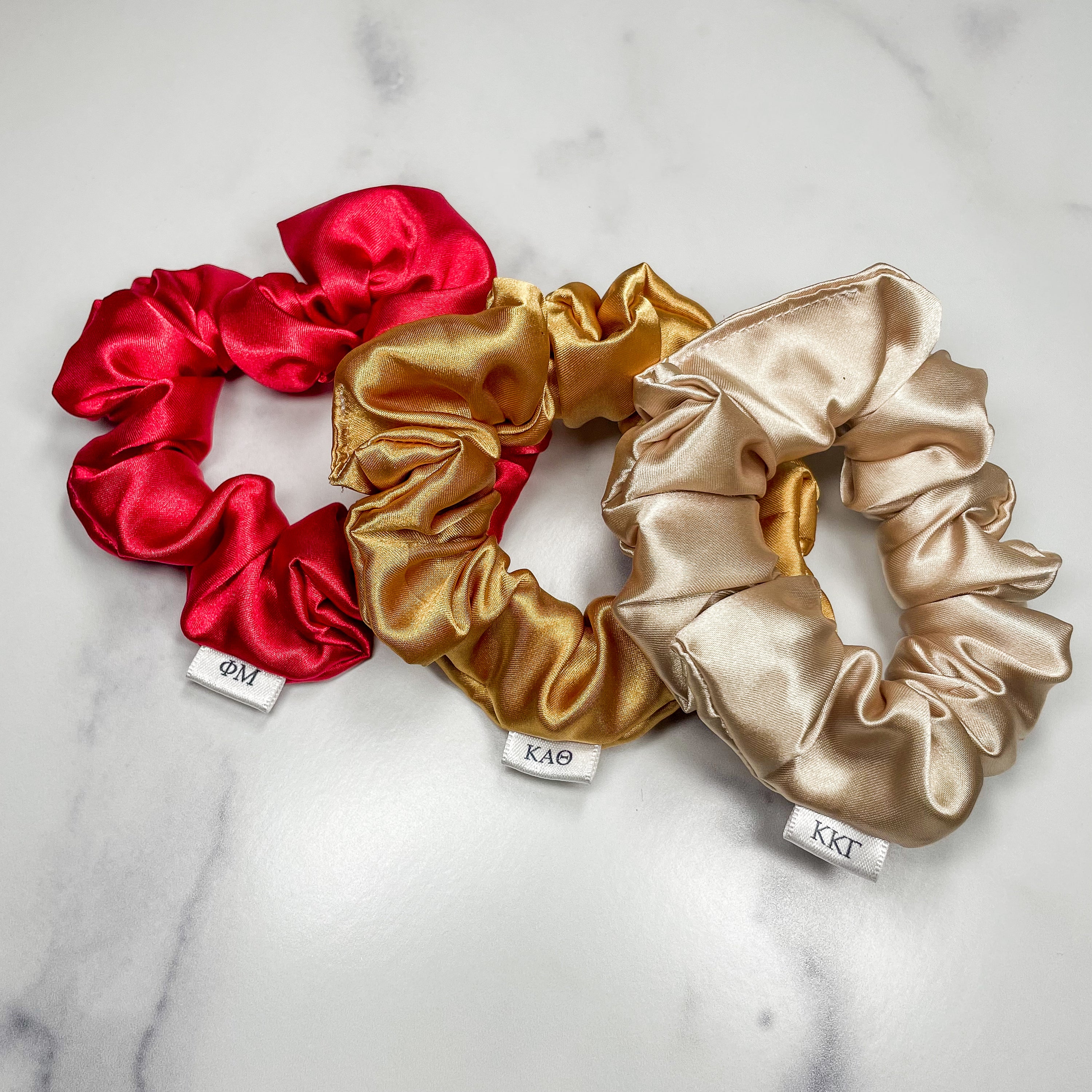 A collection of colorful sorority scrunchies featuring customizable letters, showcasing vibrant designs and soft fabric.