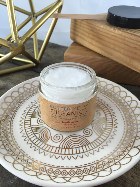 A glass jar of All Natural Organic Whitening Toothpaste with a wooden applicator, showcasing its creamy texture and natural ingredients.