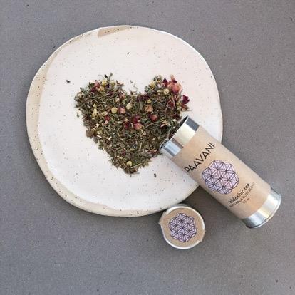 A beautifully arranged metal canister of Bliss Blend Tea, showcasing its vibrant herbal ingredients like Gotu Kola, Tulsi, and Rose, surrounded by calming floral elements.