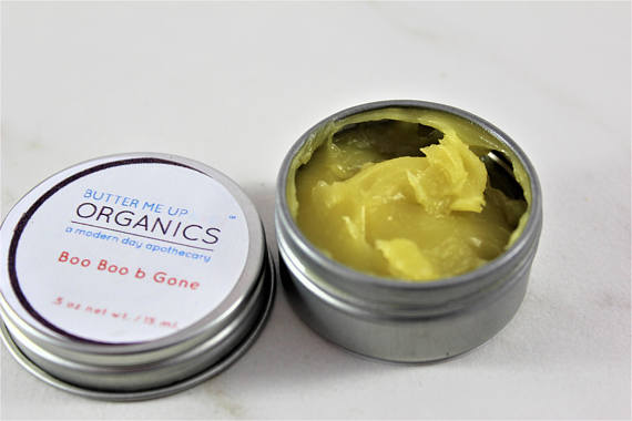 A small tin of Boo Boo b Gone natural neosporin salve, featuring a blend of organic herbal oils for healing cuts and scrapes, with a rustic design.