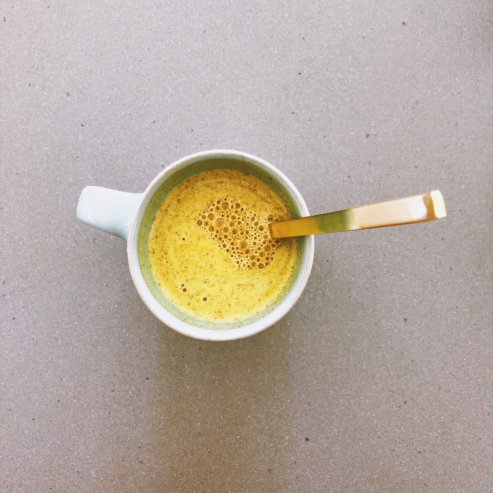 A glass jar of Golden Milk powder with a golden hue, surrounded by turmeric roots and spices, showcasing its Ayurvedic ingredients.