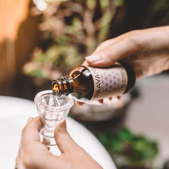 A soothing eye wash ritual kit featuring floral water, a glass eye wash cup, and a muslin travel pouch, designed for eye health and rejuvenation.