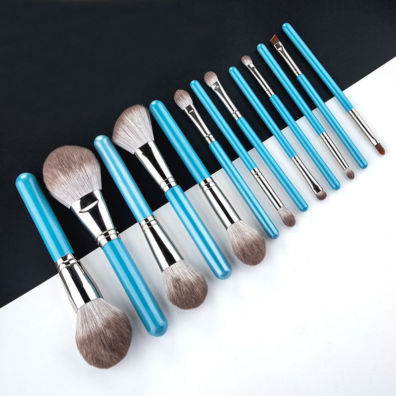 A complete set of 13 blue makeup brushes displayed in a leather tool belt, showcasing various brush types for face, eyes, and lips.