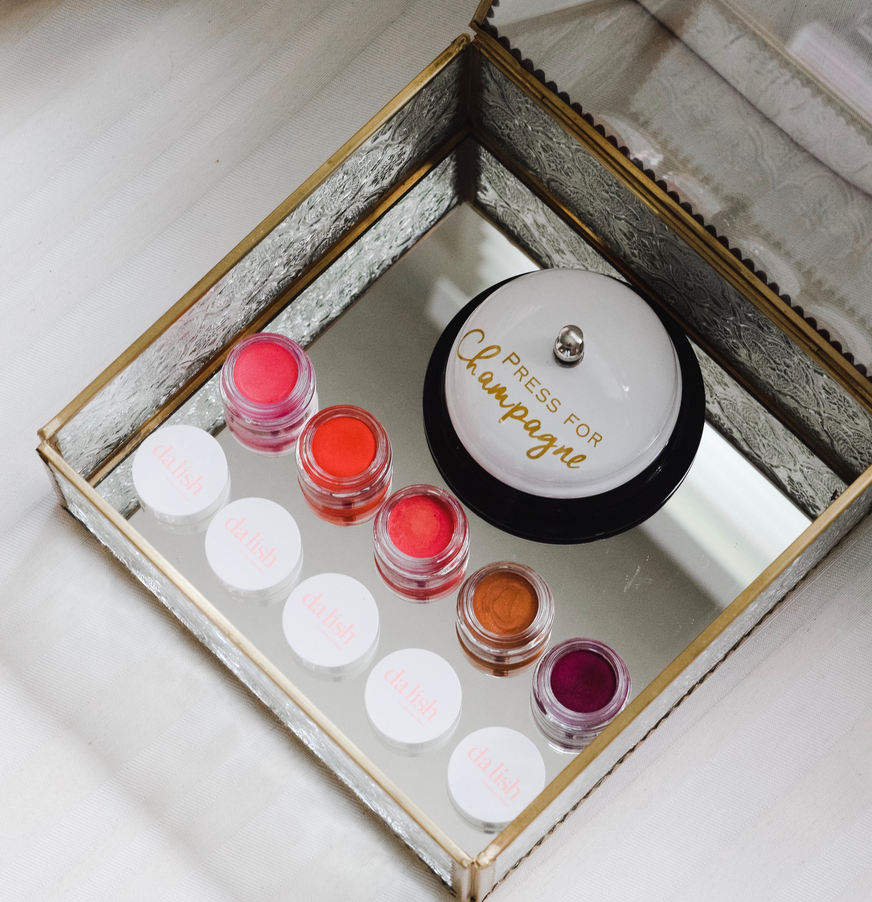 A collection of five LIP & CHEEK BALMS in vibrant shades including pink, coral, dusty rose, bronzer, and plum, displayed in elegant pots.