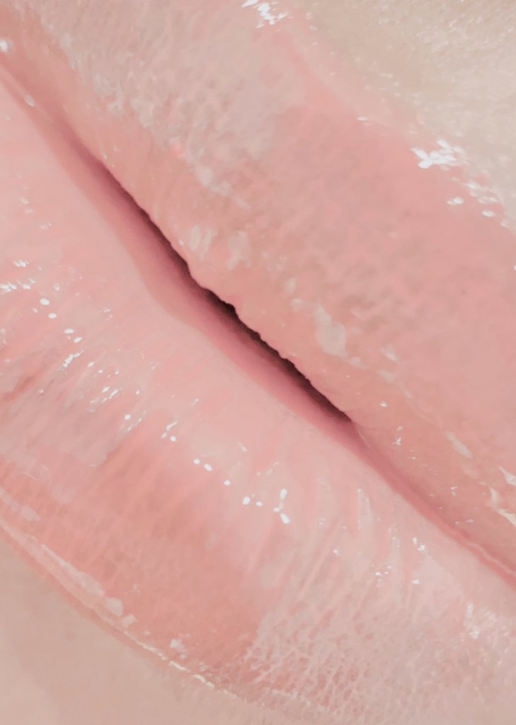 A close-up of a glossy Lip Plumper tube with a shiny applicator, showcasing its nourishing formula and vibrant color.