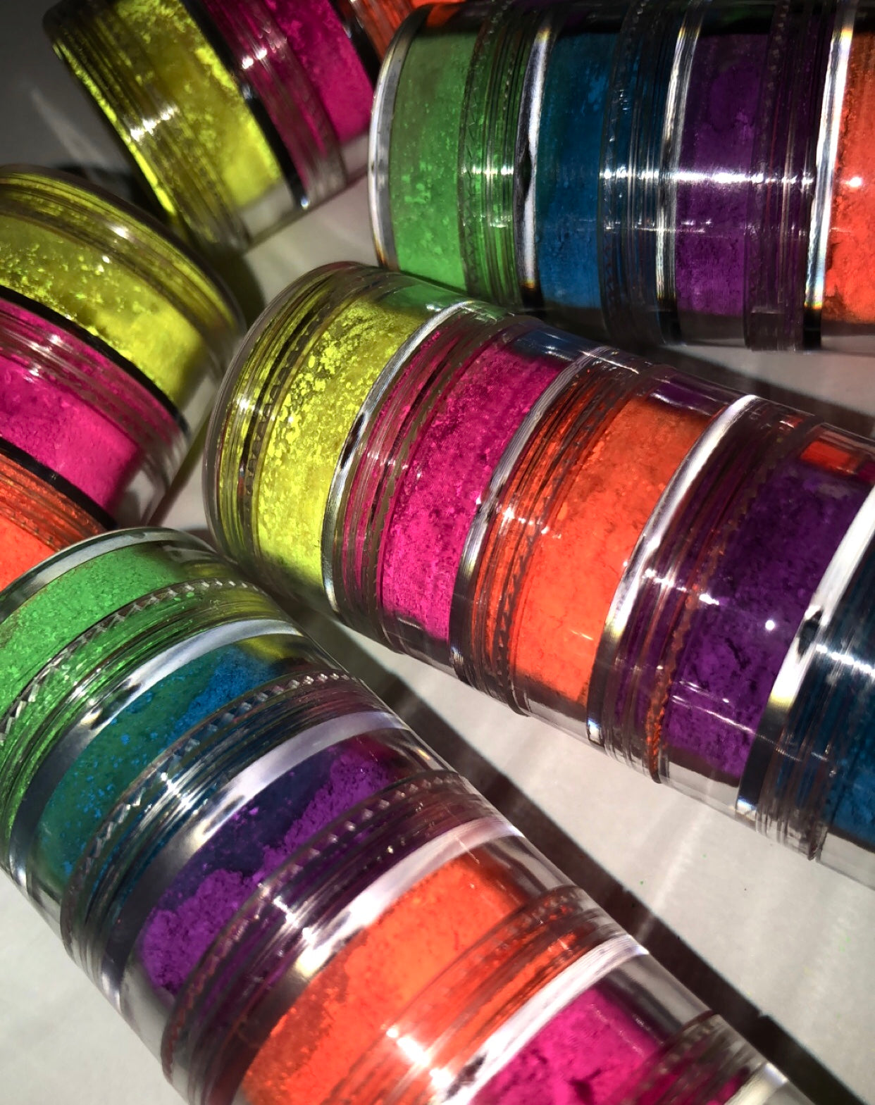 A vibrant stack of six neon pigments in assorted colors including yellow, green, pink, purple, orange, and blue, perfect for bold makeup looks.