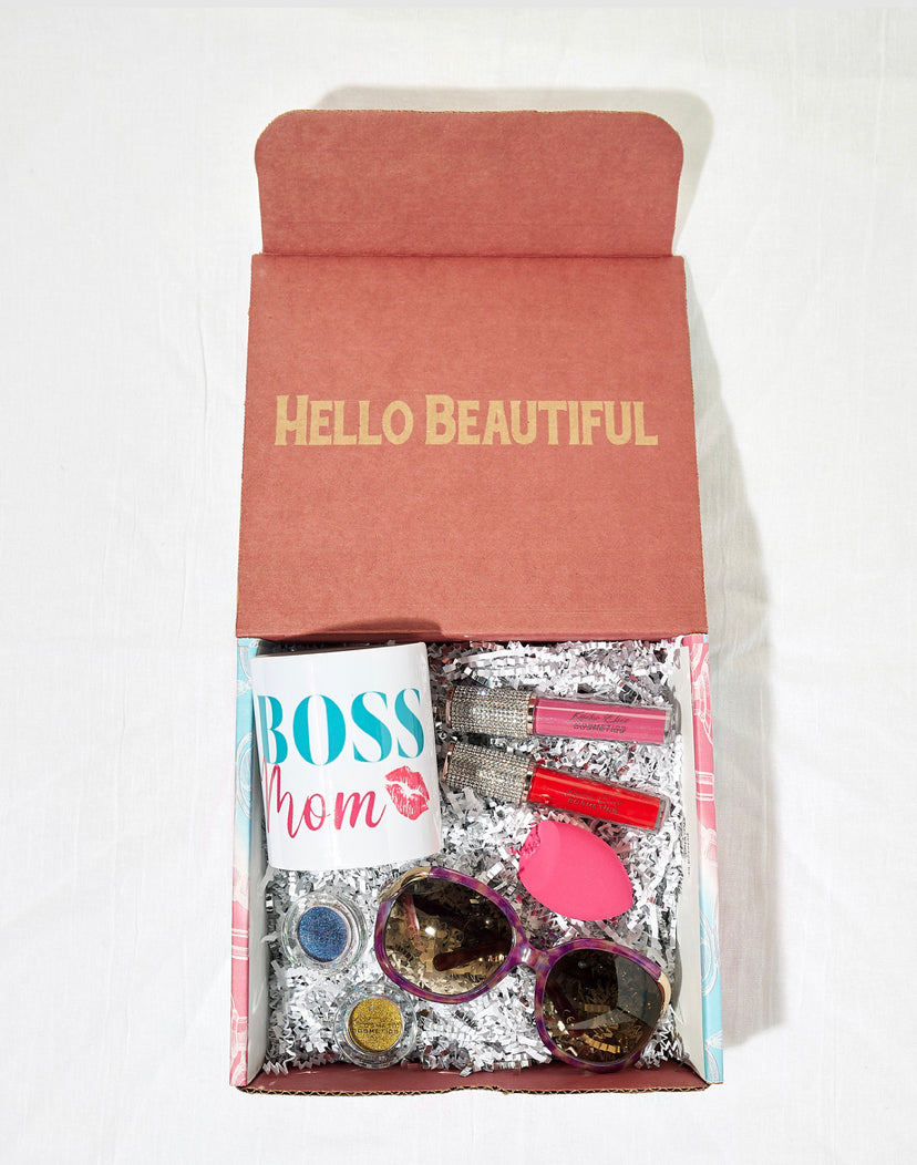 The Boss Mom Beauty Box featuring cosmetics and accessories for mothers, including a mug, sunglasses, makeup sponge, lip glosses, and eyeshadows.