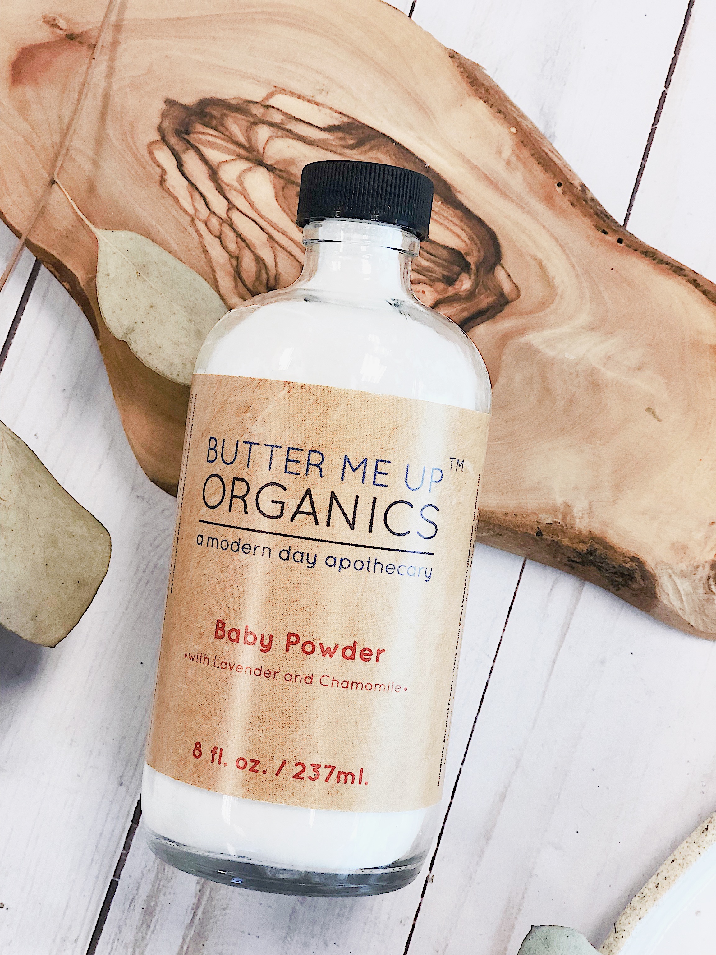 A glass bottle of All Natural Talc Free Baby Powder with organic ingredients, featuring chamomile and lavender flowers, designed for gentle baby care.