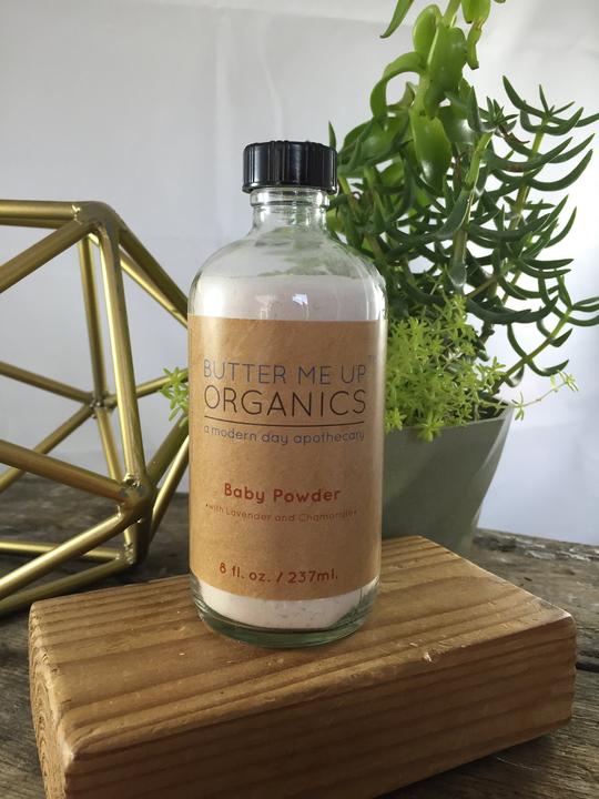 A glass bottle of All Natural Talc Free Baby Powder with organic ingredients, featuring chamomile and lavender flowers, designed for gentle baby care.