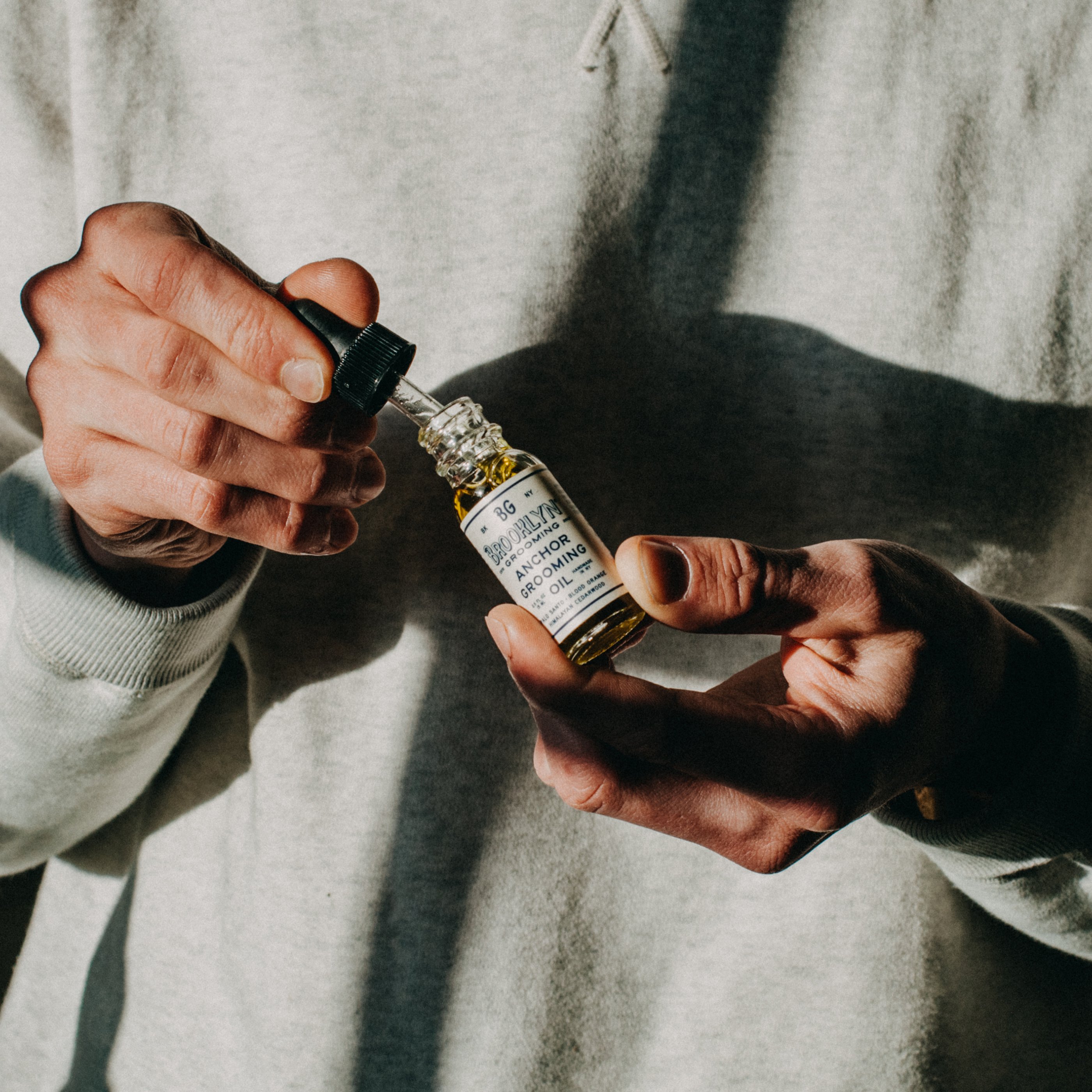 Bottle of Anchor Grooming Oil with a dropper, showcasing its light golden color and elegant design, set against a neutral background.