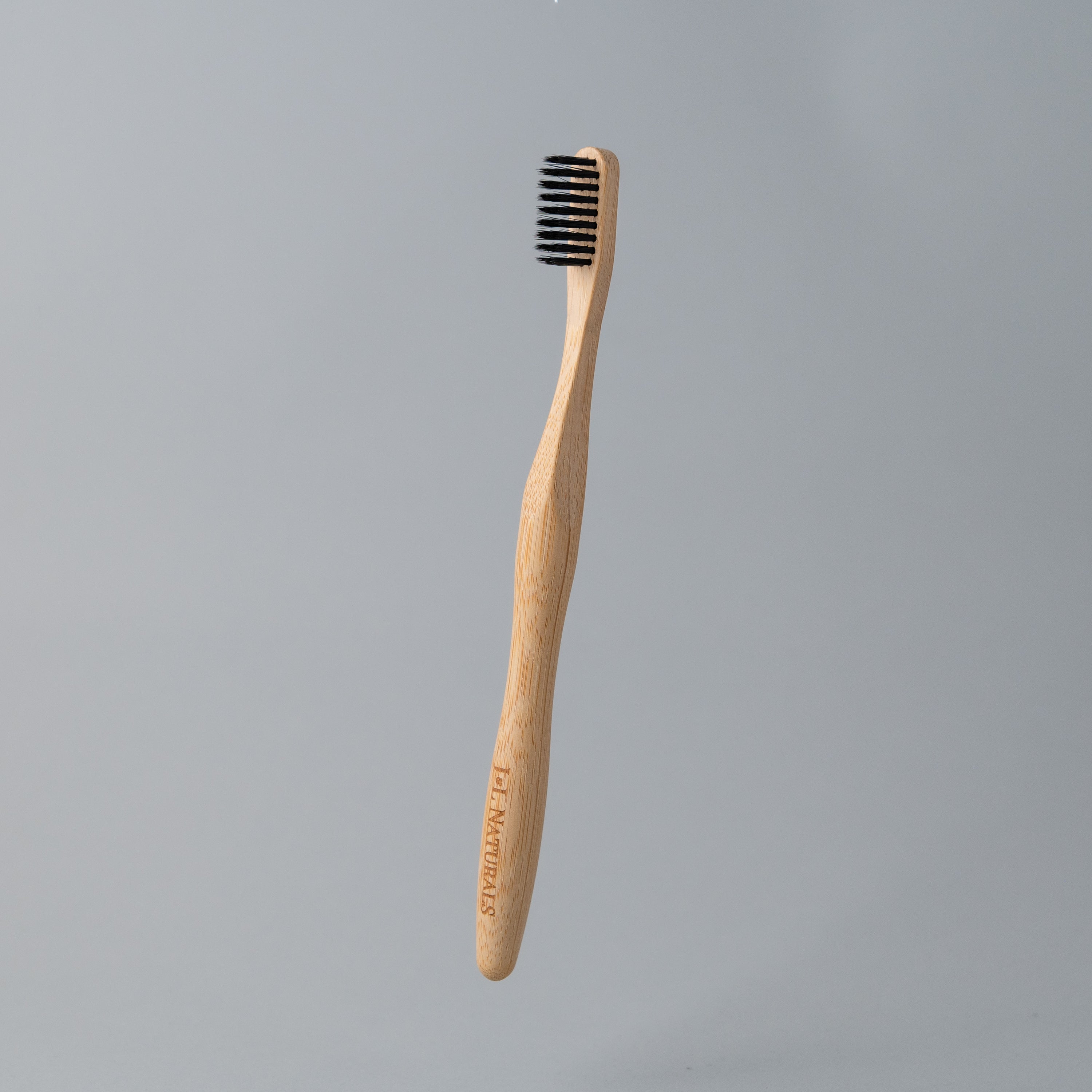 A bamboo toothbrush with medium wavy bristles and an ergonomic handle, available in various colors including black, white, natural, and rainbow.