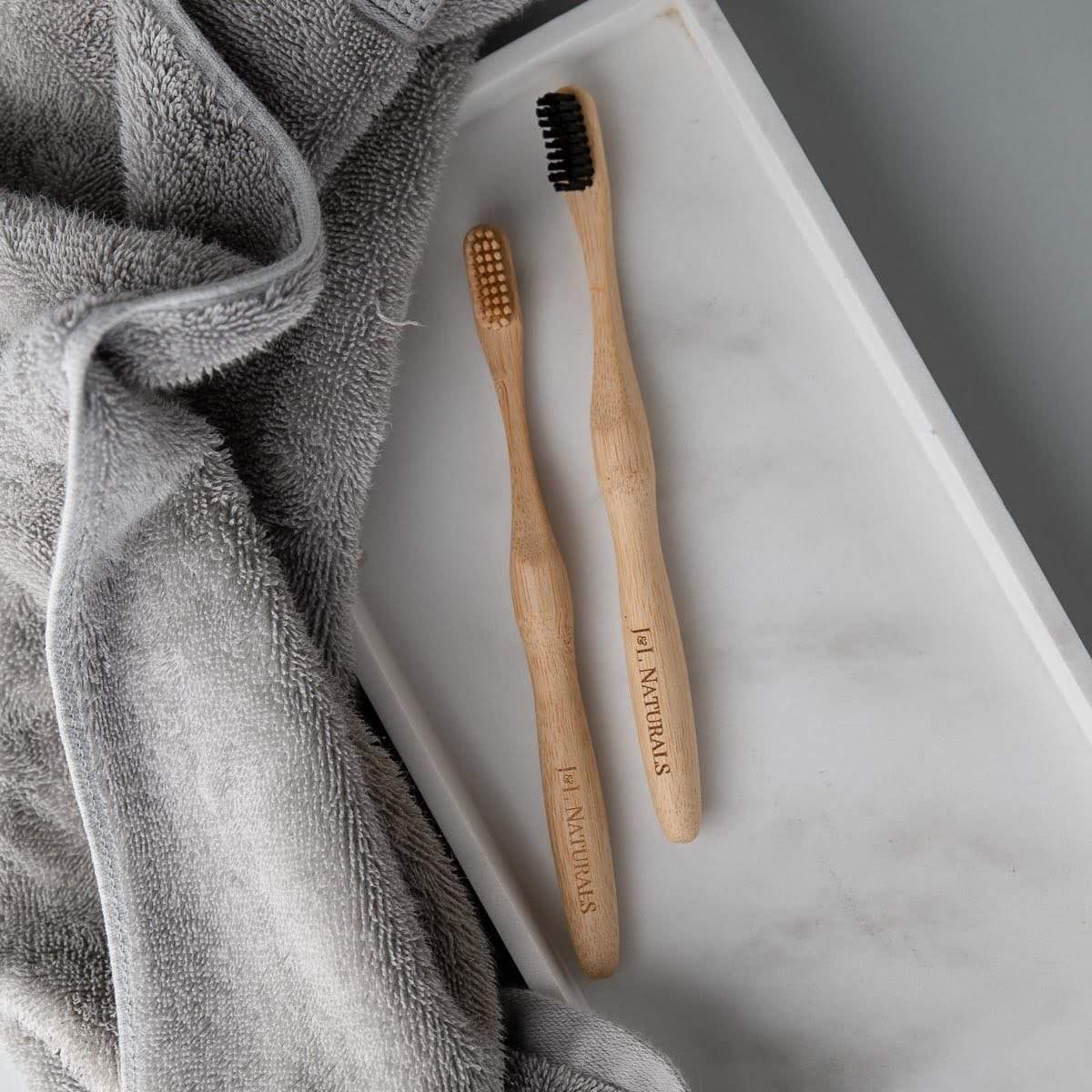 Two bamboo toothbrushes with ergonomic handles and medium wavy bristles, available in various colors.